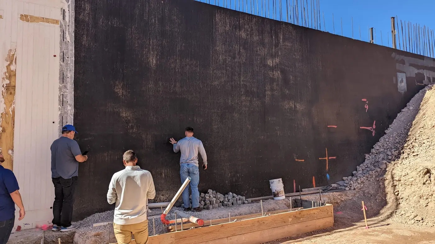 Crew inspecting a large masonry wall coated in black Wetsuit membrane